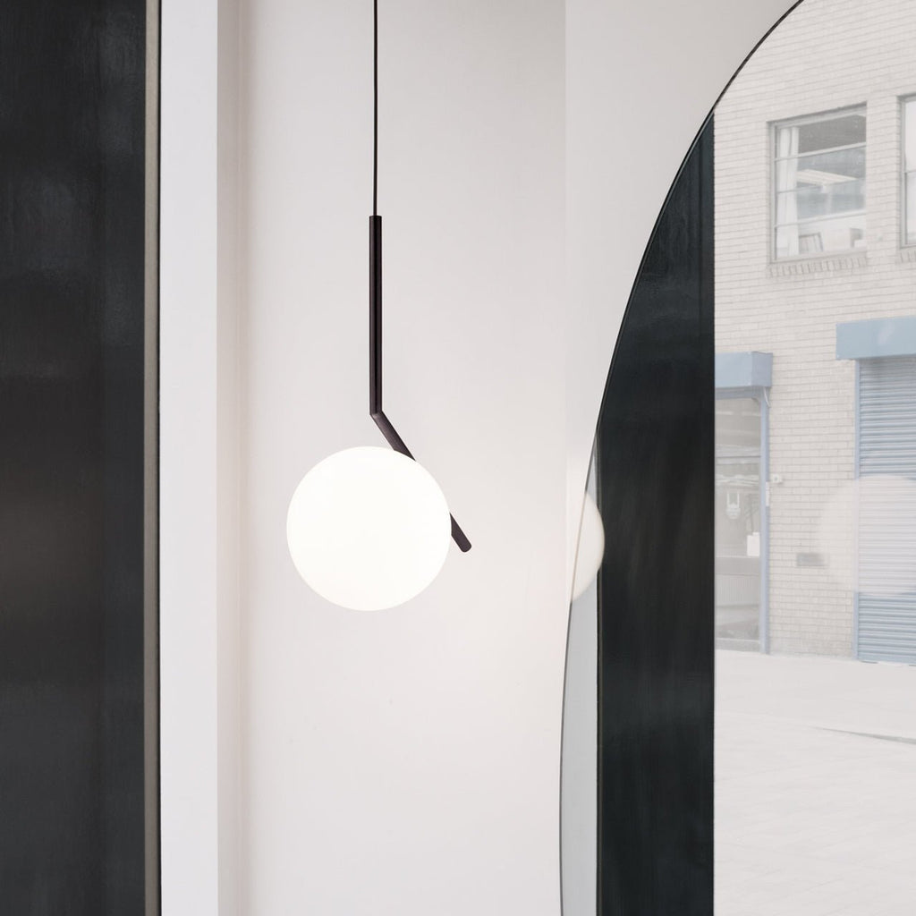 A Clérachic pendant with a black angled stem and a white glass globe, hung beside a tall arched mirror in a bright hallway.