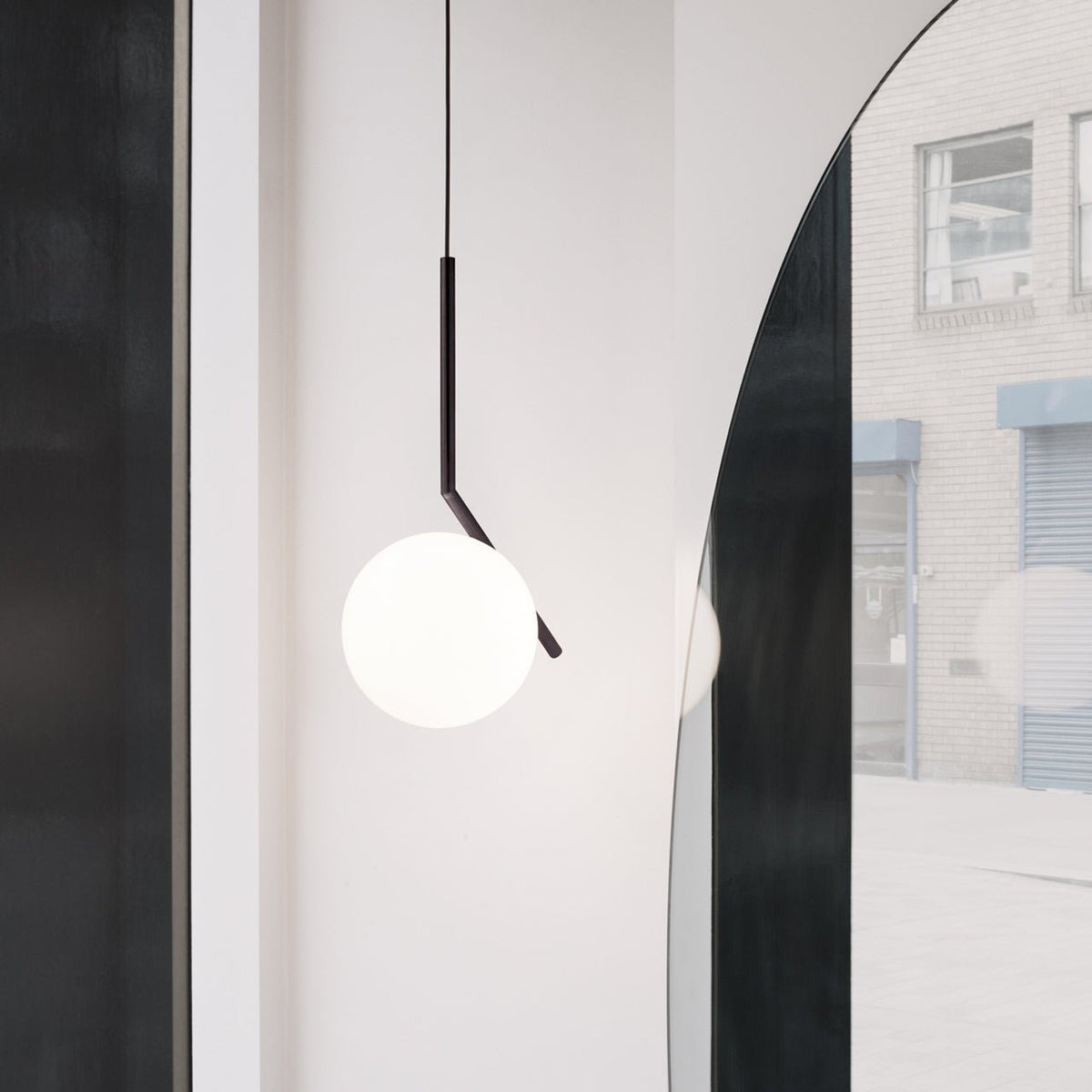 A Clérachic pendant with a black angled stem and a white glass globe, hung beside a tall arched mirror in a bright hallway.