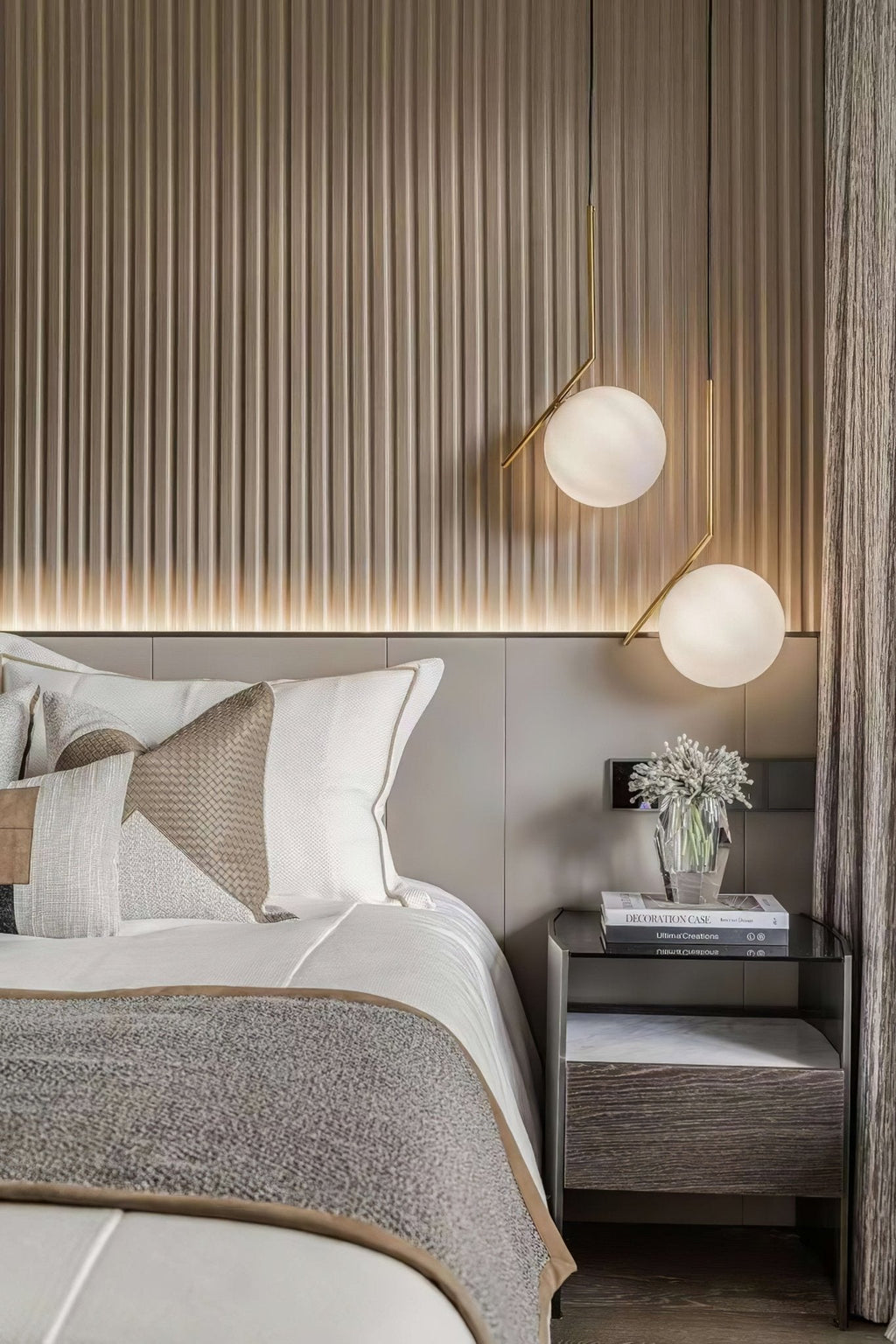 Two Clérachic globe pendants glow above matching bedside tables, set against a pale fluted wall panel and layered grey bedding.