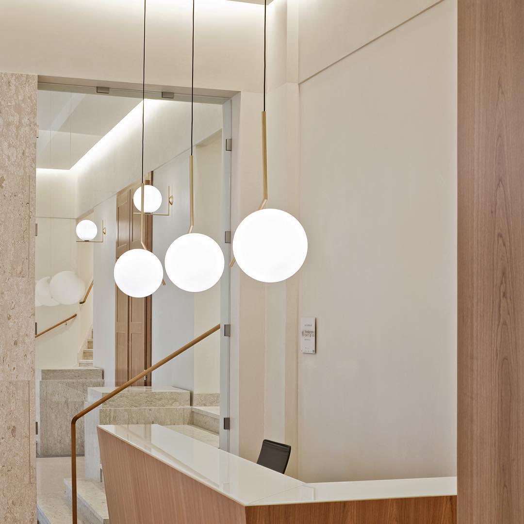 Three Clérachic globe pendants at different heights hang in a pale stone entrance hall, beside a timber reception counter.