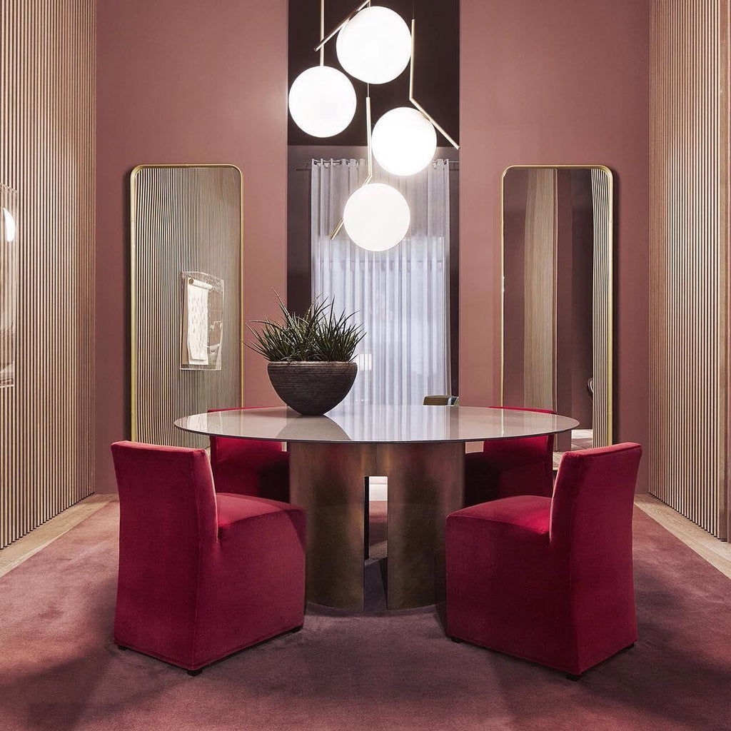A cluster of four Clérachic globe pendants at staggered heights hangs over a round table with red upholstered chairs.
