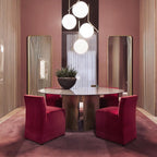 A cluster of four Clérachic globe pendants at staggered heights hangs over a round table with red upholstered chairs.