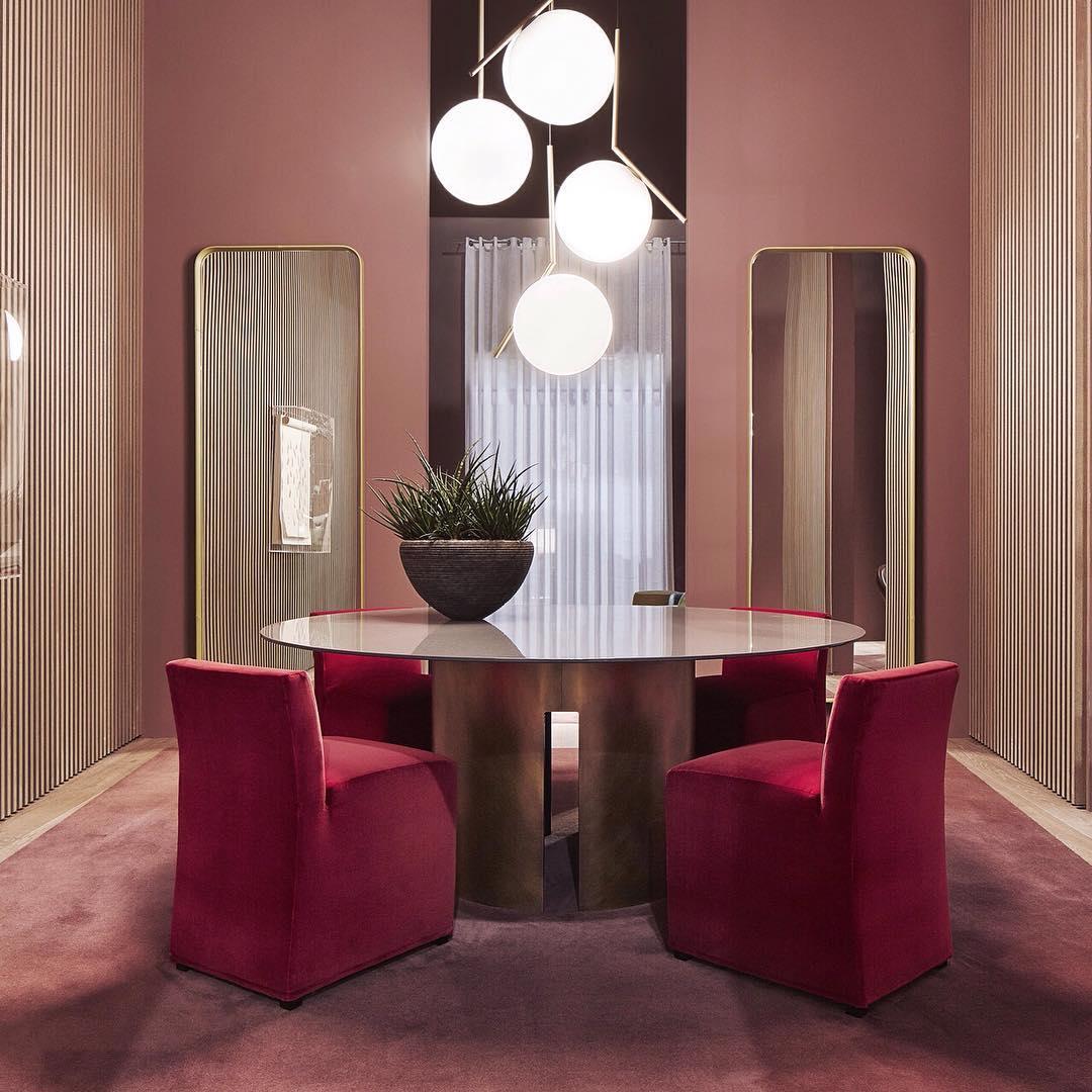 A cluster of four Clérachic globe pendants at staggered heights hangs over a round table with red upholstered chairs.