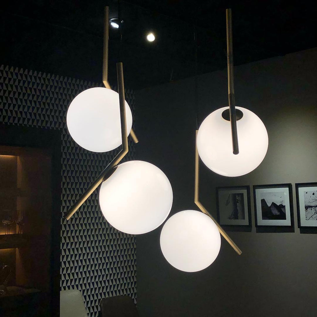 Four Clérachic globe pendants glow against a dark patterned wall, with brass and black stems angled in different directions.