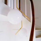 Looking up a white stairwell beside a wooden handrail, two Clérachic globe pendants of different sizes hang from brass stems.