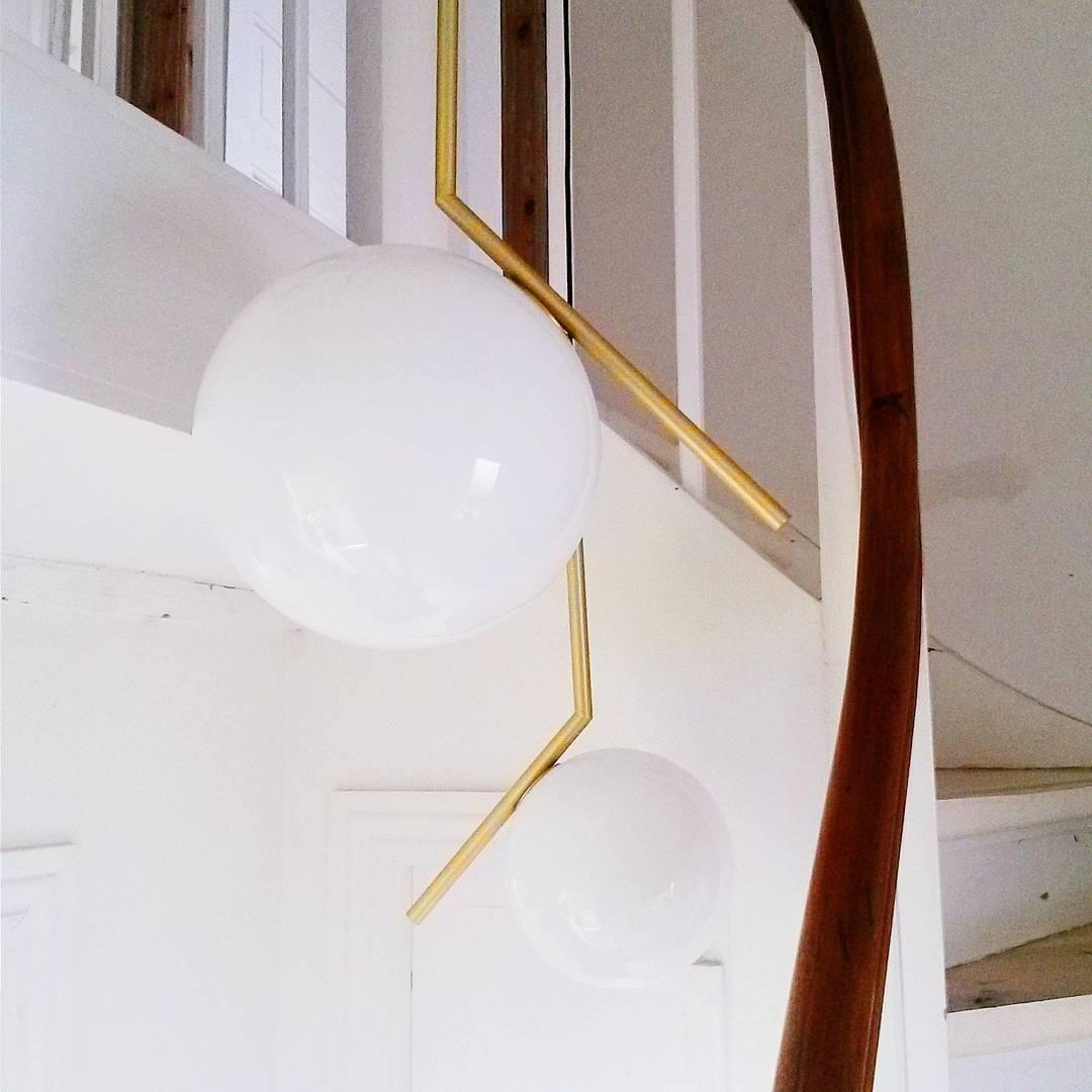 Looking up a white stairwell beside a wooden handrail, two Clérachic globe pendants of different sizes hang from brass stems.