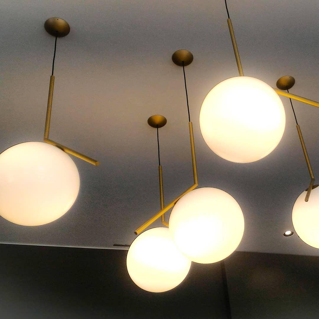 Close under a dark ceiling, several Clérachic globe pendants glow warm yellow, each with a brass stem and a round canopy.
