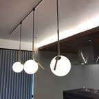 Three Clérachic globe pendants of different sizes hang from a ceiling track above a dark kitchen, the nearest one brightly lit.