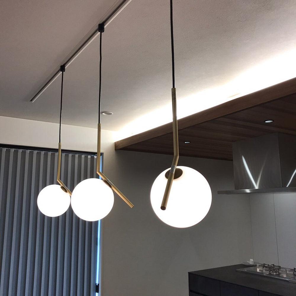 Three Clérachic globe pendants of different sizes hang from a ceiling track above a dark kitchen, the nearest one brightly lit.