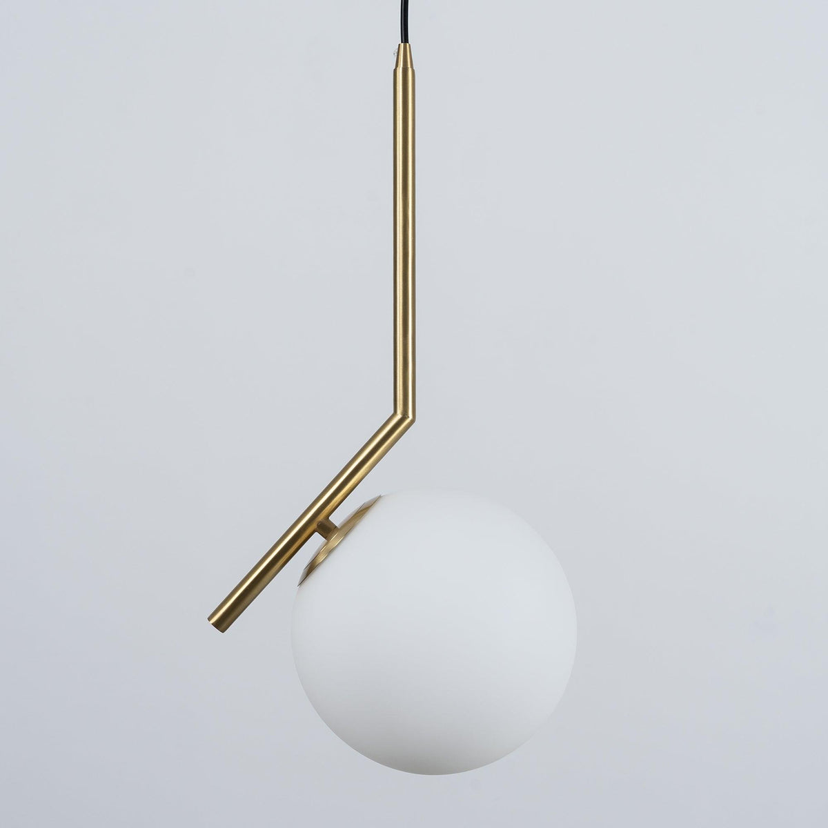 Studio view of a Clérachic pendant on a soft grey backdrop, with a brass stem bent at an angle above a matt white glass globe.