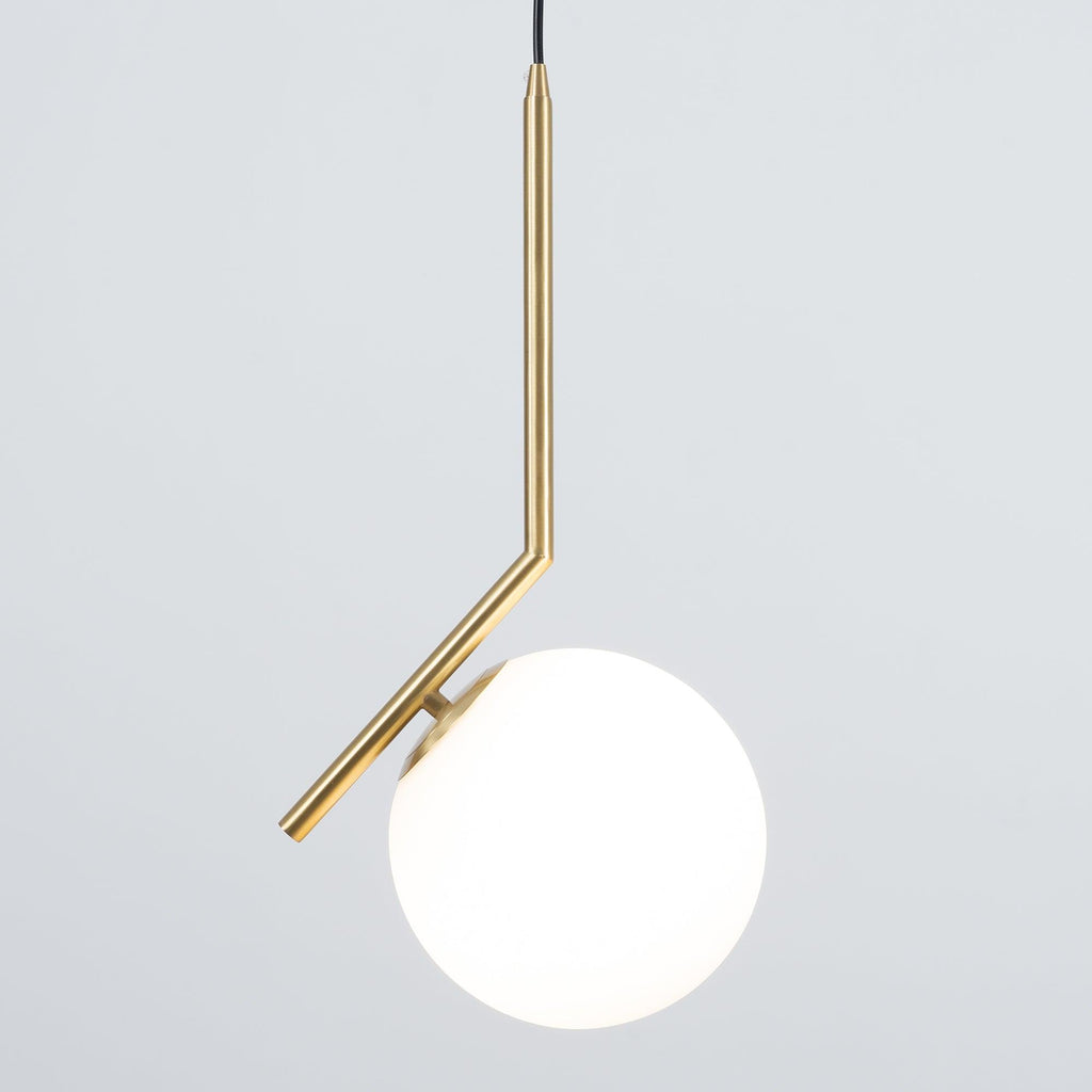 A Clérachic pendant on grey, lit from within so the white globe glows beside the brass stem and its small round cap.