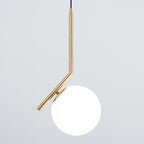 A Clérachic pendant on grey, lit from within so the white globe glows beside the brass stem and its small round cap.