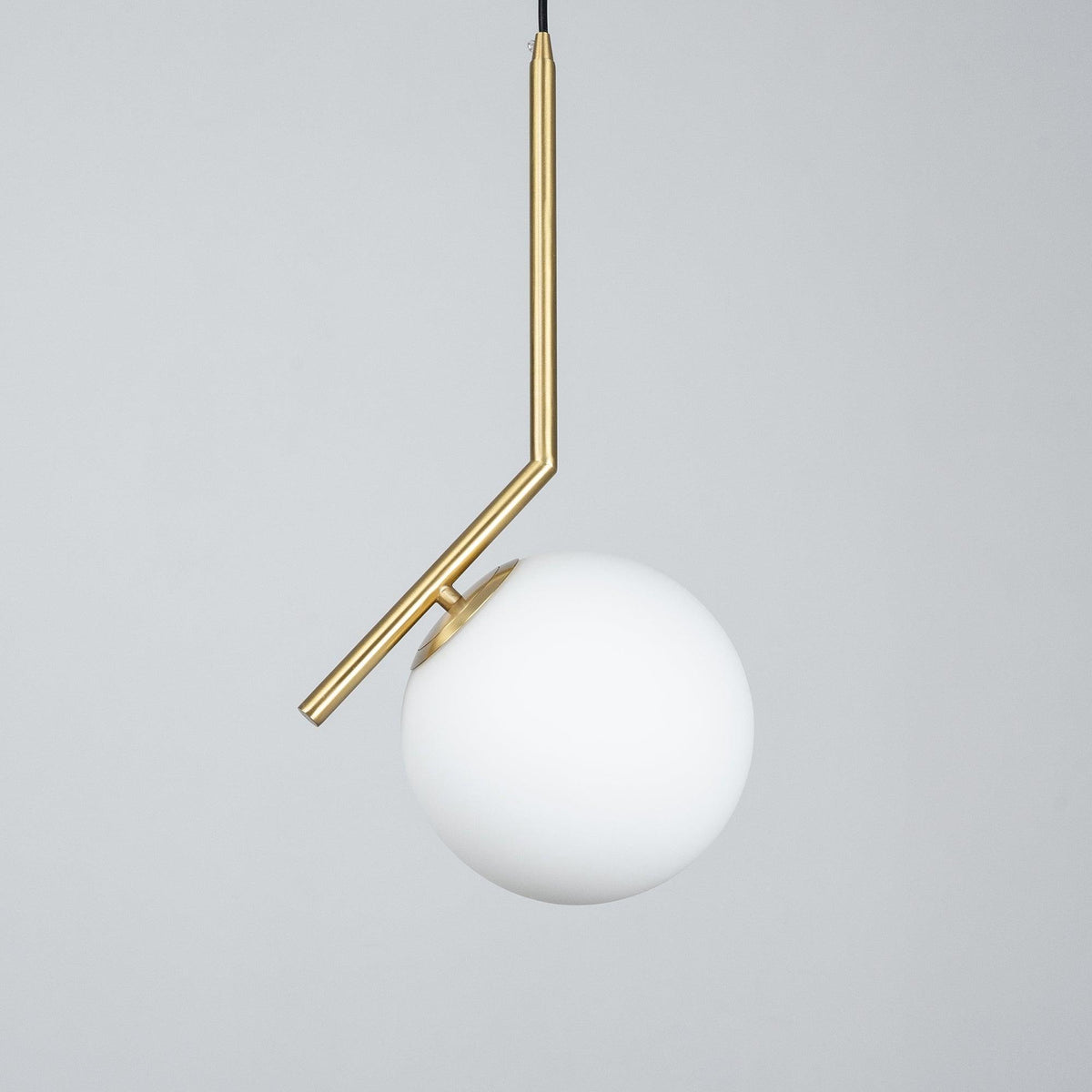 Unlit Clérachic globe pendant on a grey studio backdrop, with a slim brass stem and a smooth, matt white glass ball.
