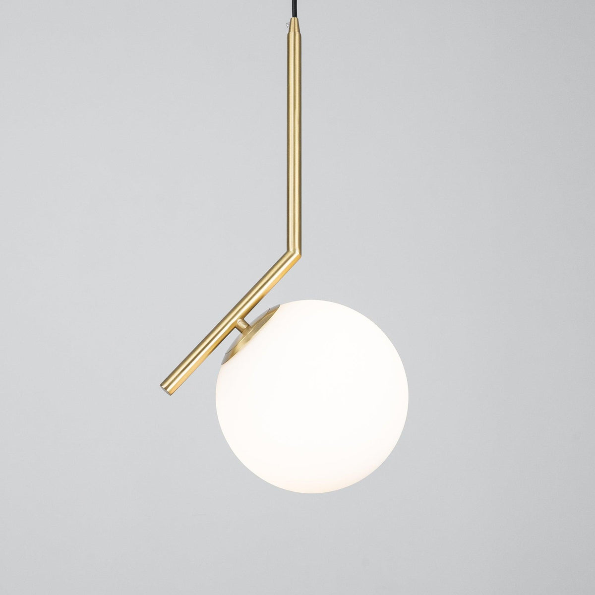 A Clérachic globe pendant on grey, turned on so the white glass glows a warm cream beside the angled brass stem.