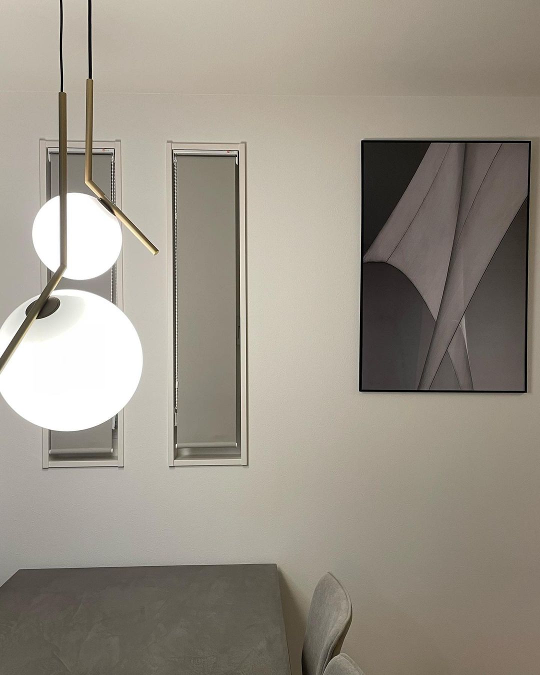 Two white globes of different sizes from this Clérachic pendant range hang on the left of a cream wall, beside a framed grey print.