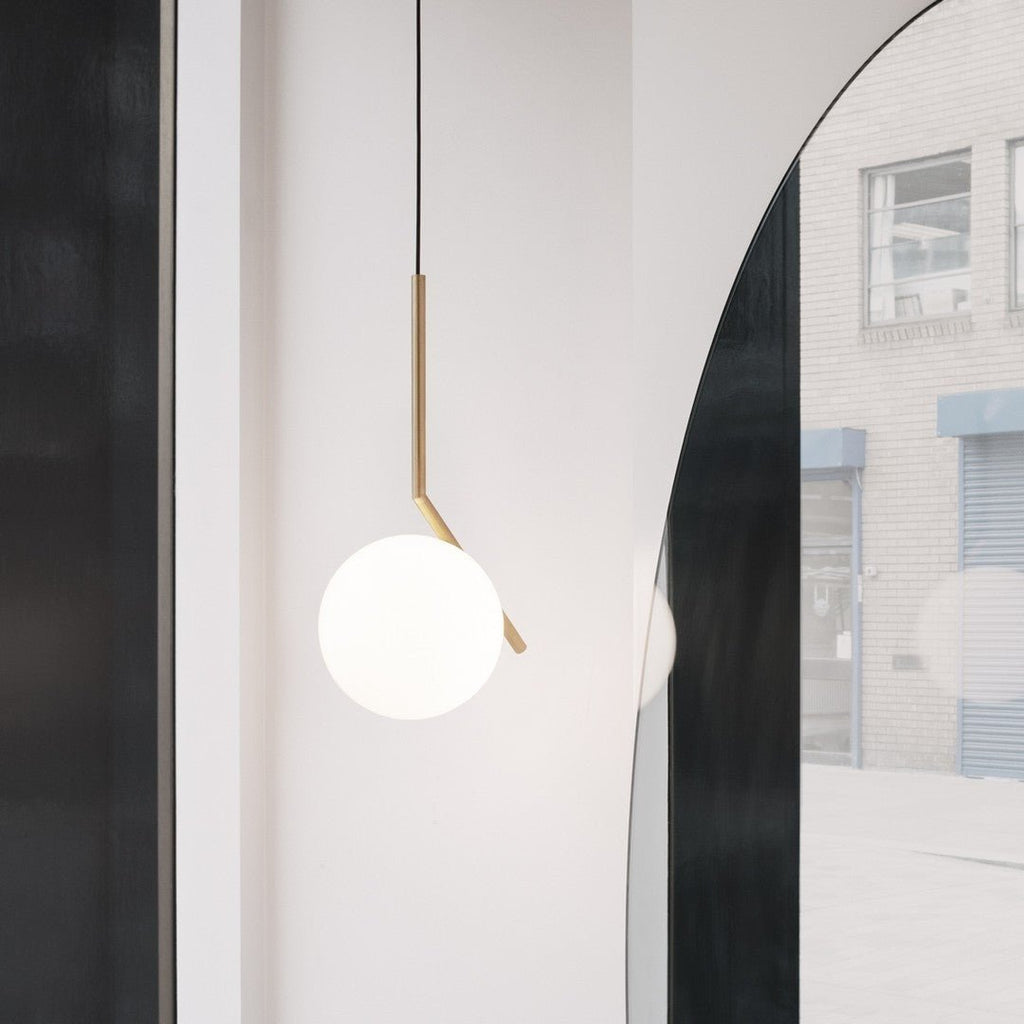 A Clérachic pendant with a brass stem and white glass globe hangs next to a tall arched mirror in a bright, minimal hallway.
