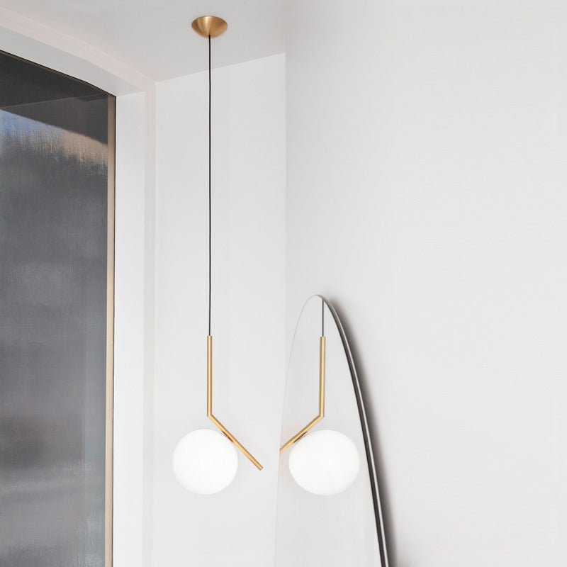 Two Clérachic pendants with brass stems hang in a white corner, one reflected in a curved mirror leaning on the wall.