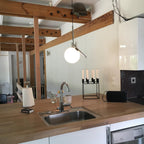 A Clérachic globe pendant hangs over a beech worktop and steel sink, with a candle holder and exposed timber beams behind.