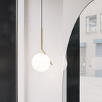A Clérachic pendant with a brass stem and white globe hangs against a pale wall, with an arched mirror reflecting the street.