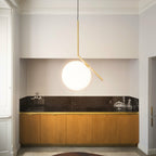 A Clérachic globe pendant with a brass stem hangs in a plaster-moulded alcove above a dark stone counter and warm oak cabinets.