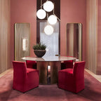 Four lit Clérachic globe pendants cluster above a round glass-topped table in a dusky rose dining room with red chairs.