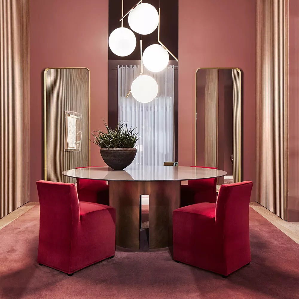 Four lit Clérachic globe pendants cluster above a round glass-topped table in a dusky rose dining room with red chairs.
