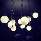 Many lit Clérachic globe pendants at varied heights fill a navy room, their brass stems angled over round white shades.