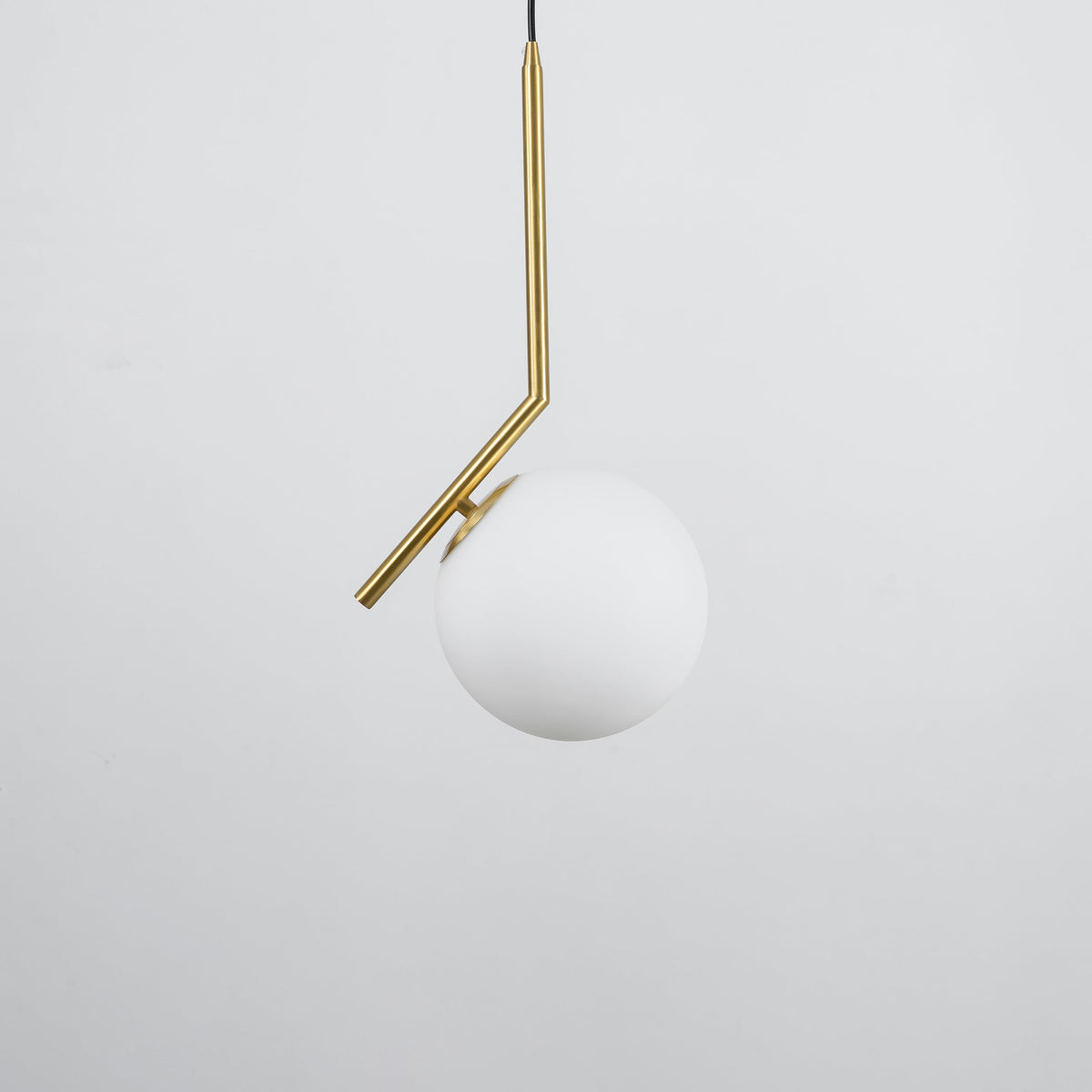 A Clérachic globe pendant on a pale grey backdrop, with a brass stem and a matt white glass ball hanging off-centre.