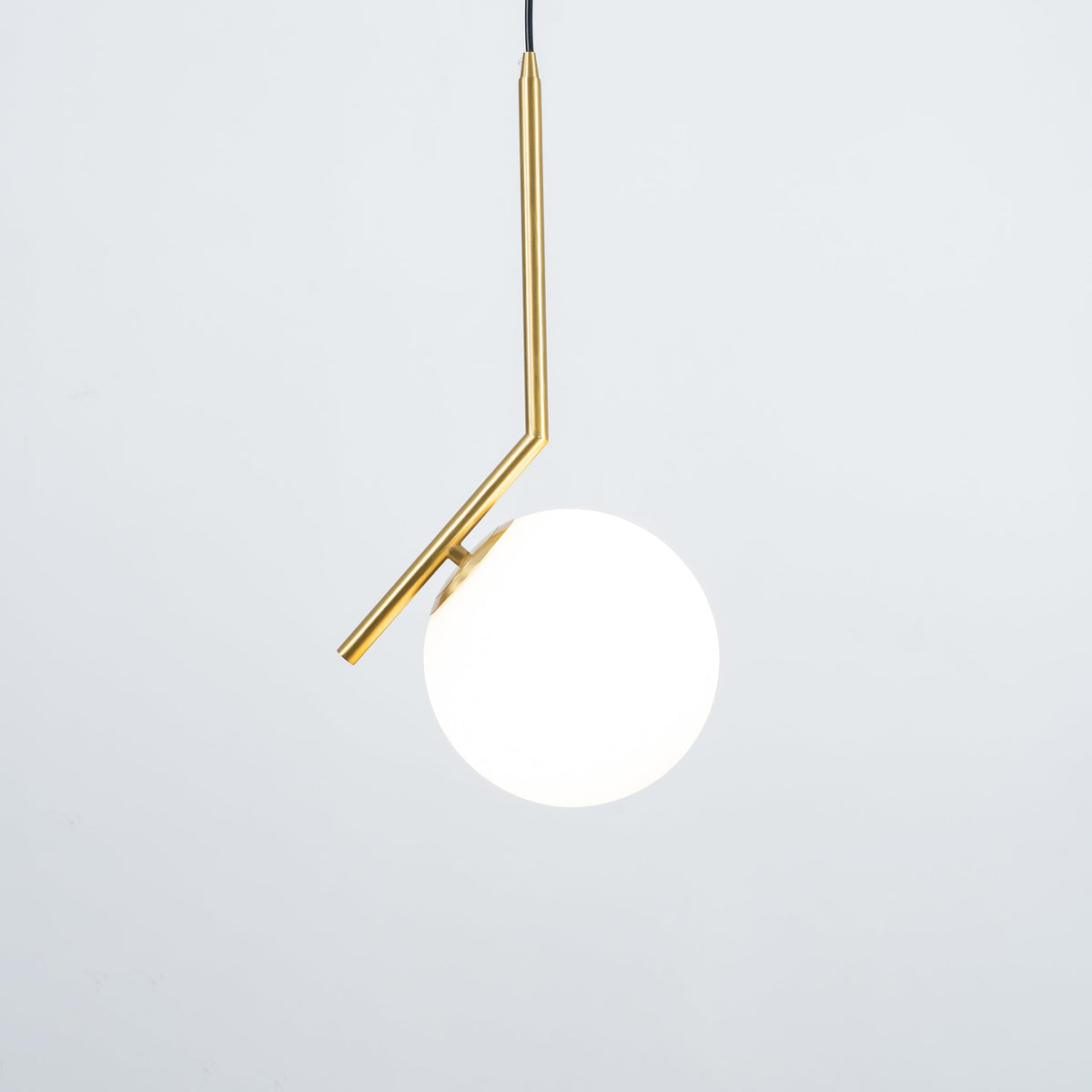 A Clérachic globe pendant lit against a pale grey-blue backdrop, with a thin brass stem and a round brass cap at the glass.