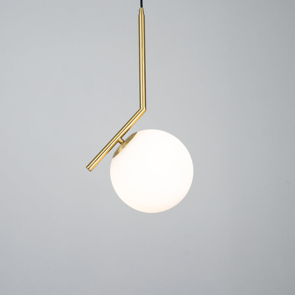 Lit Clérachic pendant on a mid-grey studio backdrop, with a bright white globe and a brass stem that bends above it.