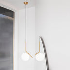 A Clérachic pendant with a brass canopy and thin black cord hangs in a white corner, with a second globe reflected in a mirror.