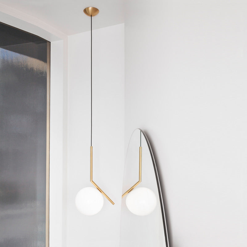 A Clérachic pendant with a brass canopy and thin black cord hangs in a white corner, with a second globe reflected in a mirror.