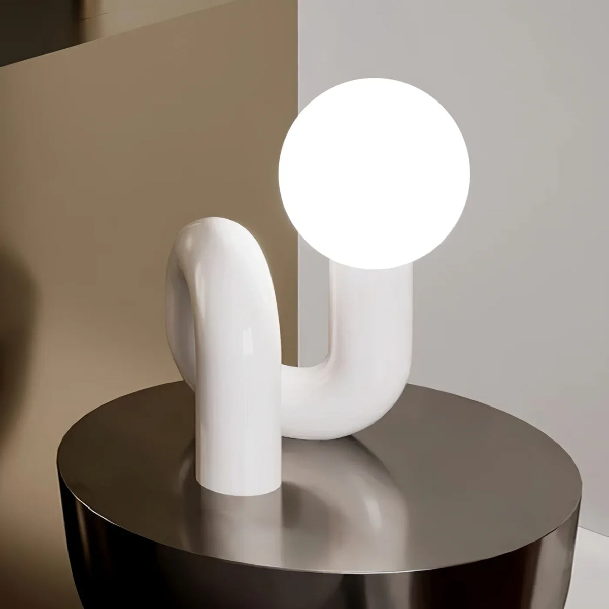 White Clérachic table lamp on a round metallic side table, its curved tube base arching under a lit globe.
