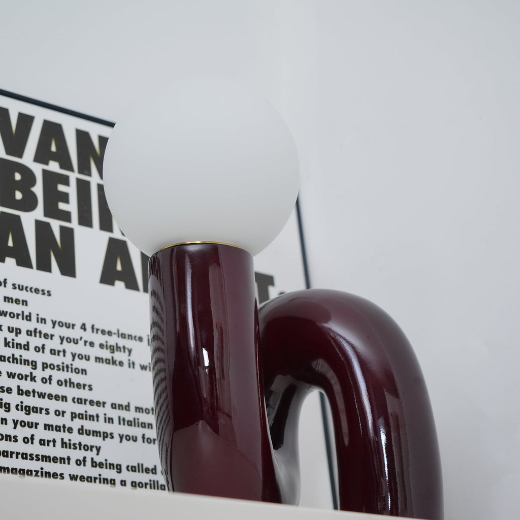 Close view of a glossy dark red Clérachic lamp base curving beneath a frosted white globe.