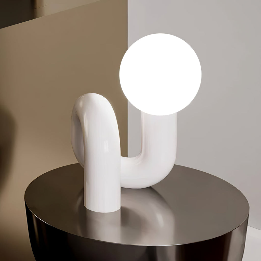 White Clérachic lamp with a lit globe above its smooth arching base, on a round dark metal table.