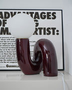 Dark red Clérachic table lamp unlit on a pale shelf, its glossy curved base reflected in the surface.