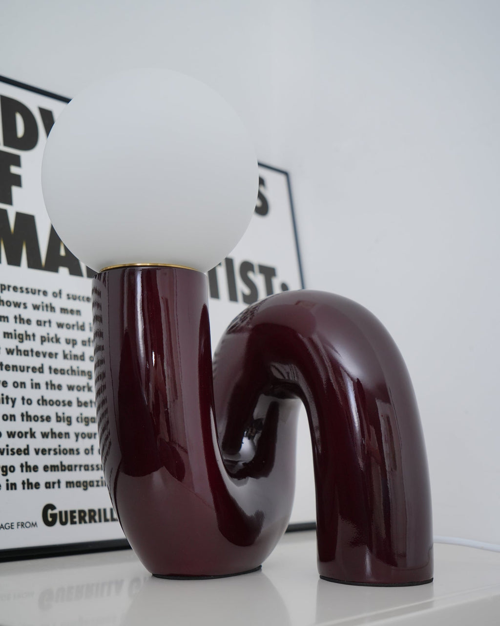 Glossy dark red Clérachic table lamp in close view, the frosted globe above a looping tube base.