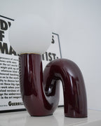 Glossy dark red Clérachic table lamp in close view, the frosted globe above a looping tube base.