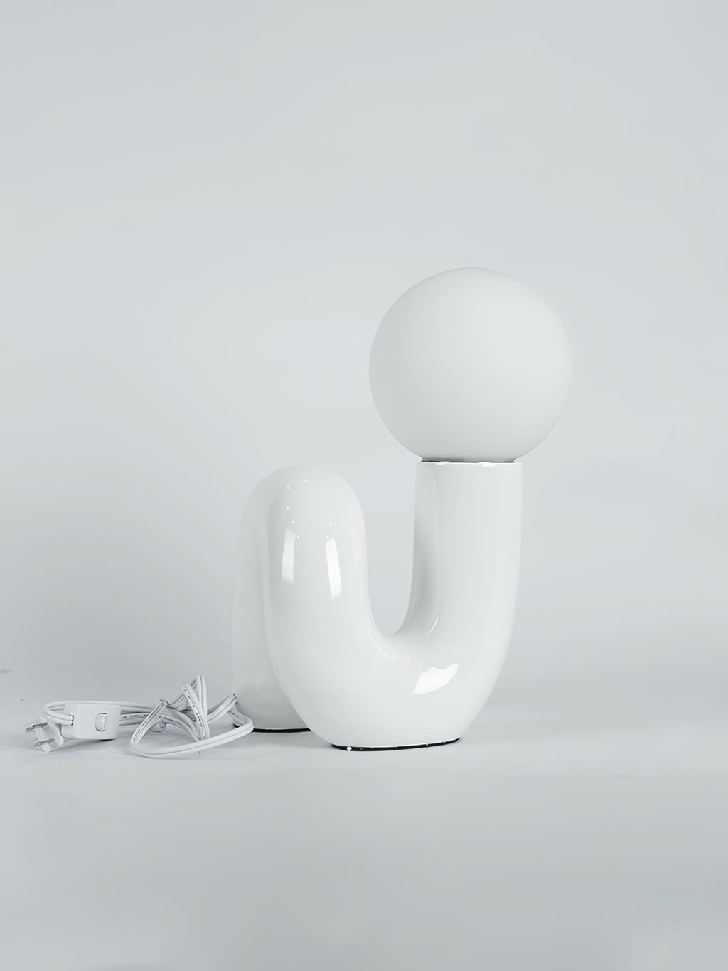 White Clérachic table lamp on a pale backdrop, its white cord and switch coiled on the floor at the left.