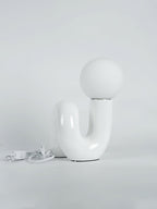 White Clérachic table lamp on a pale backdrop, its white cord and switch coiled on the floor at the left.