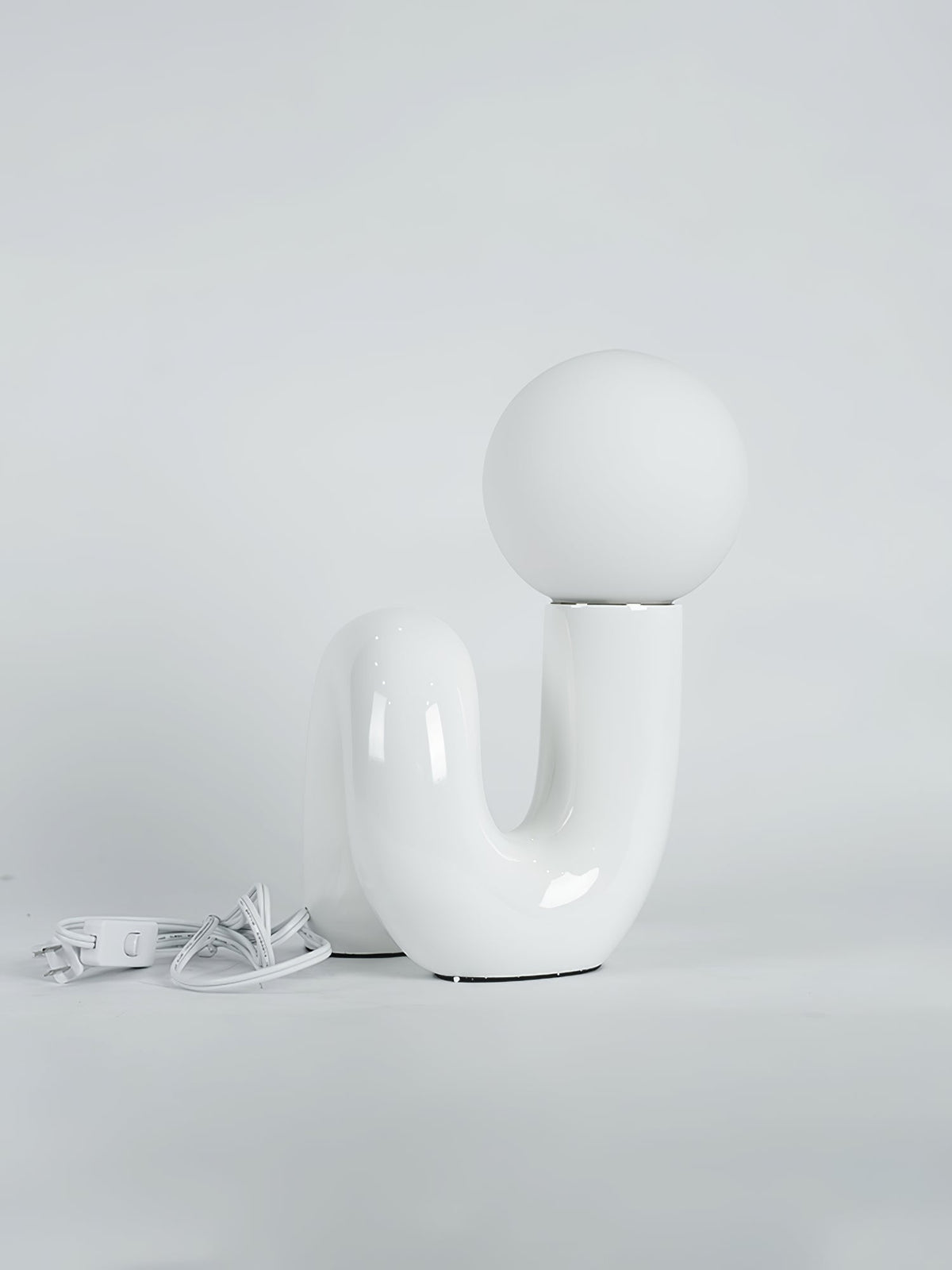 White Clérachic table lamp on a pale backdrop, its white cord and switch coiled on the floor at the left.