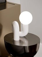 White Clérachic table lamp with a glowing globe on a black round table in a muted bedroom corner.