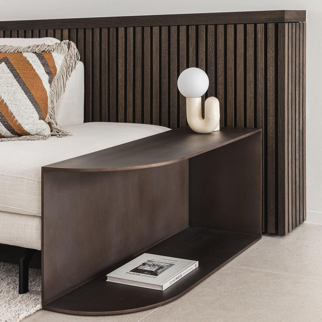 Cream Clérachic table lamp on a dark wooden shelf by a sofa, with striped cushions and a slatted headboard.