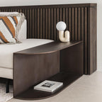 Cream Clérachic table lamp on a dark wooden shelf by a sofa, with striped cushions and a slatted headboard.
