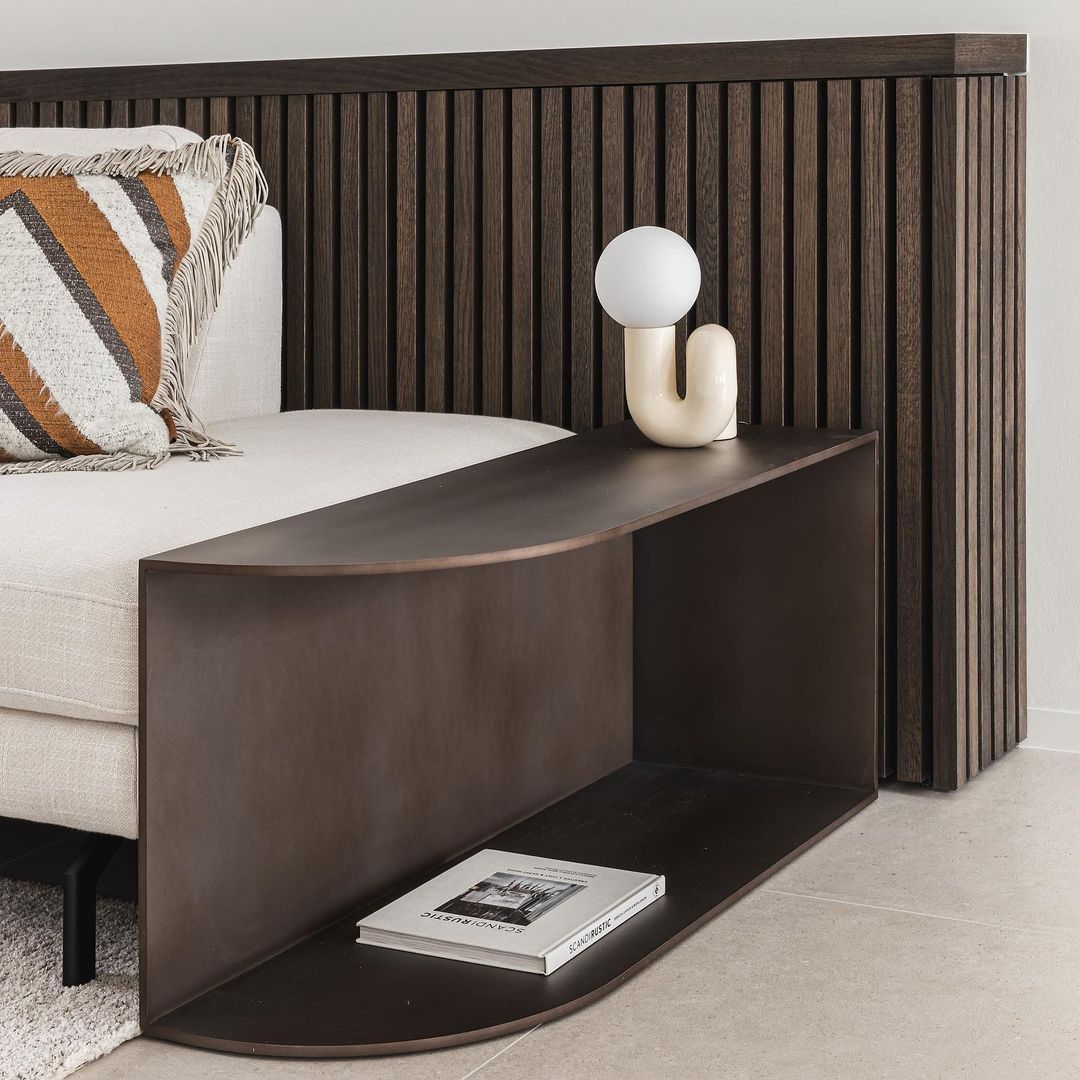 Cream Clérachic table lamp on a dark wooden shelf by a sofa, with striped cushions and a slatted headboard.