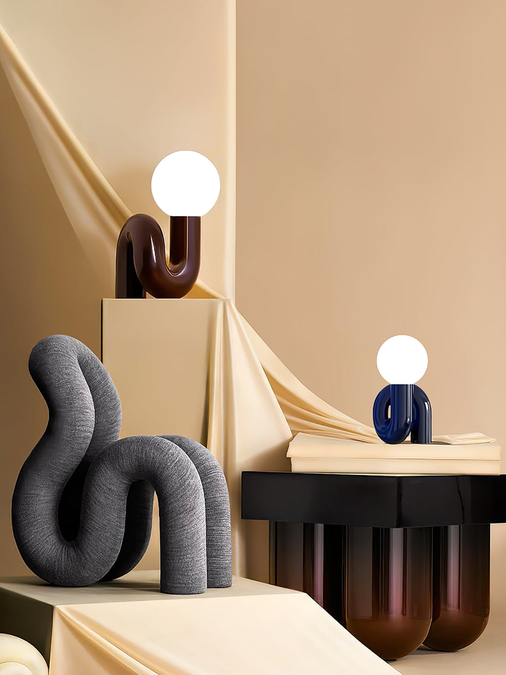 Dark red and blue Clérachic globe lamps on a staged set of cream plinths, with a grey sculpture to the left.
