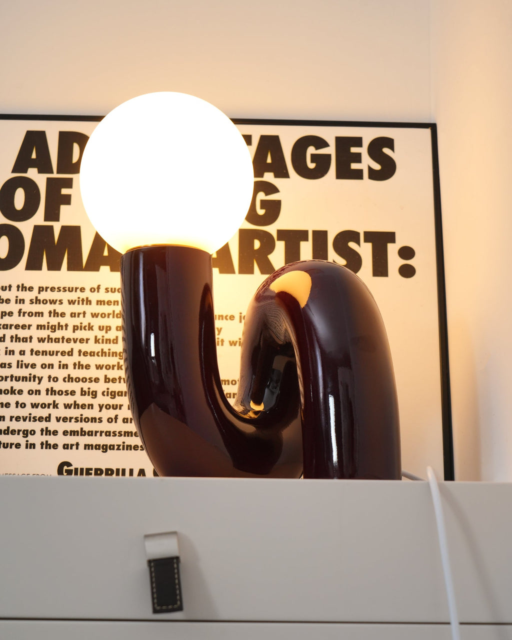 Lit dark red Clérachic table lamp, its globe bright and a warm glow showing in the base opening.