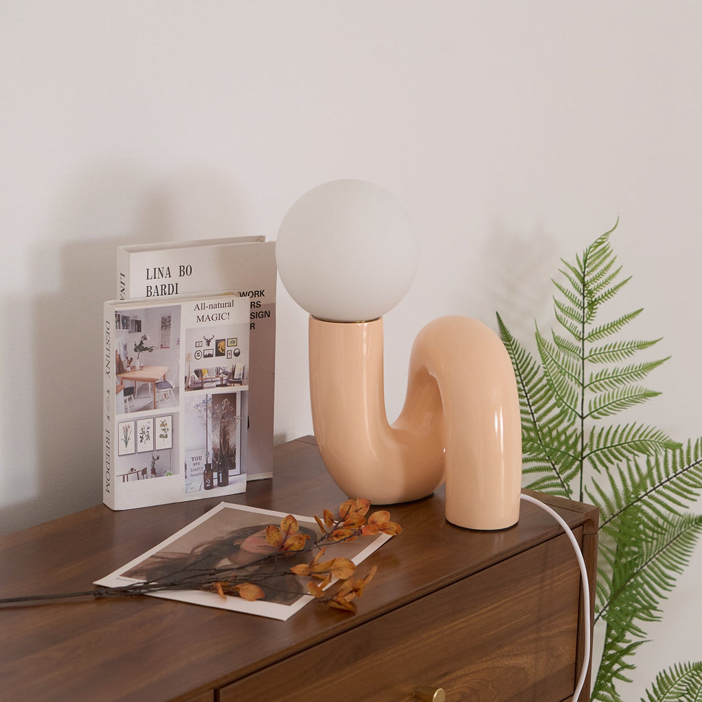 Peach Clérachic table lamp on a walnut chest, with a fern, a book and dried leaves around it.