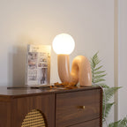 Peach Clérachic table lamp lit on a walnut cabinet with a cane panel, a fern and a book beside it.