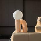 Peach Clérachic table lamp perched on a leather sofa arm, the curved base facing the dark wall behind.